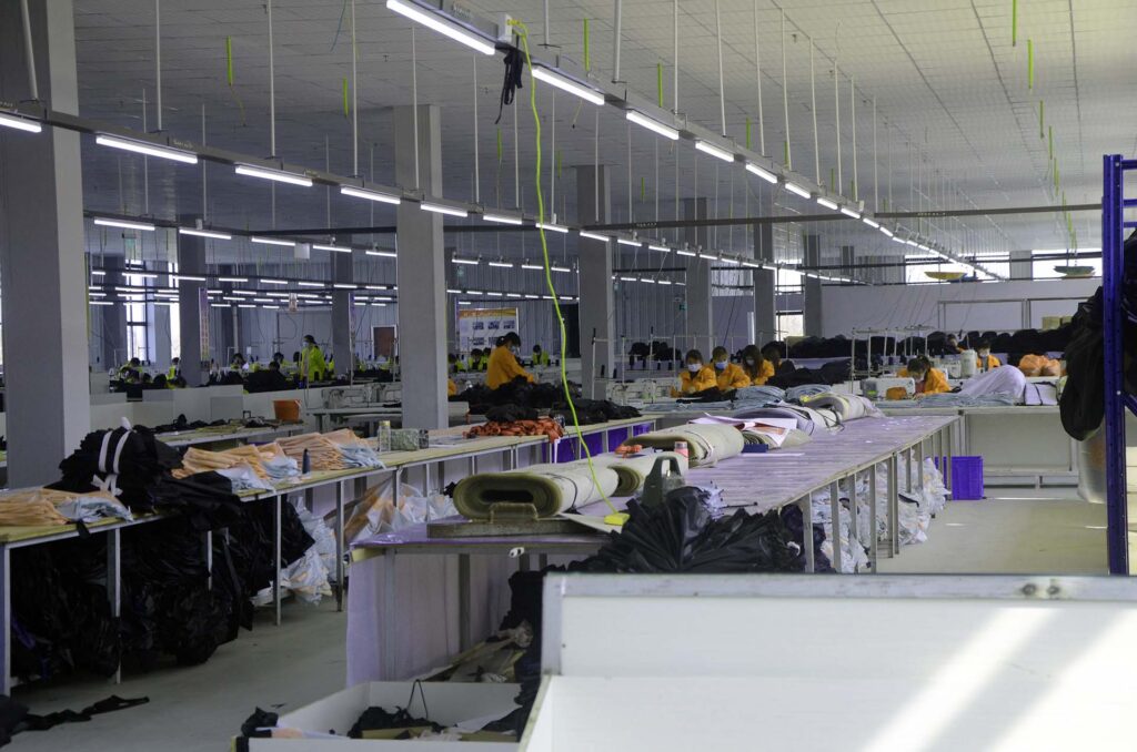 Large workshop with rows of work tables, rolls of fabric and workers in yellow jackets