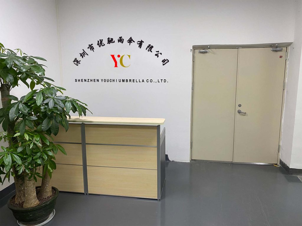 Reception desk below a wall sign reading Shenzhen Youchi Umbrella Co., Ltd. with the YC logo